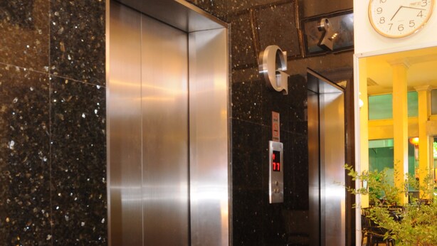 A modern elevator with a digital display, a marble wall, and a potted plant. - Lodge 61 Bed & Breakfast (Bangkok)