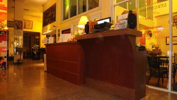 A hotel reception area with a wooden reception desk, a clock, and a window with a view of the street.