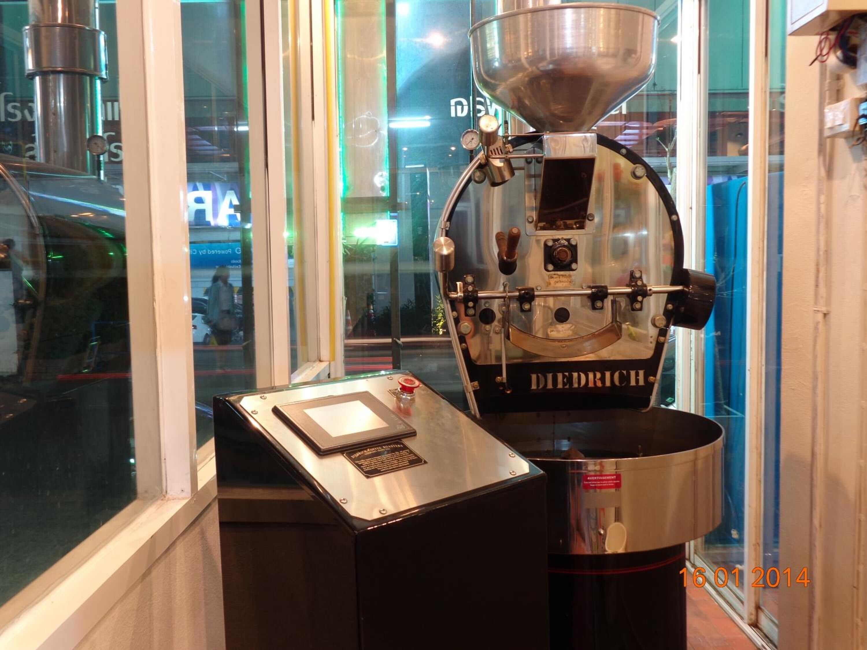 A coffee roasting machine with a digital interface, placed in a glass-fronted room.