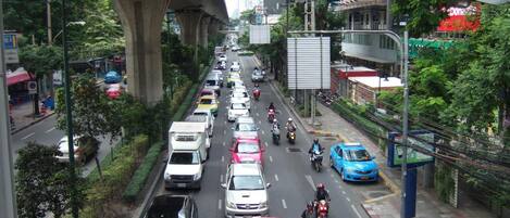 Une rue animée en milieu urbain, avec plusieurs voies de circulation, où l’on croise des voitures et des motos, et qui passe sous un pont.