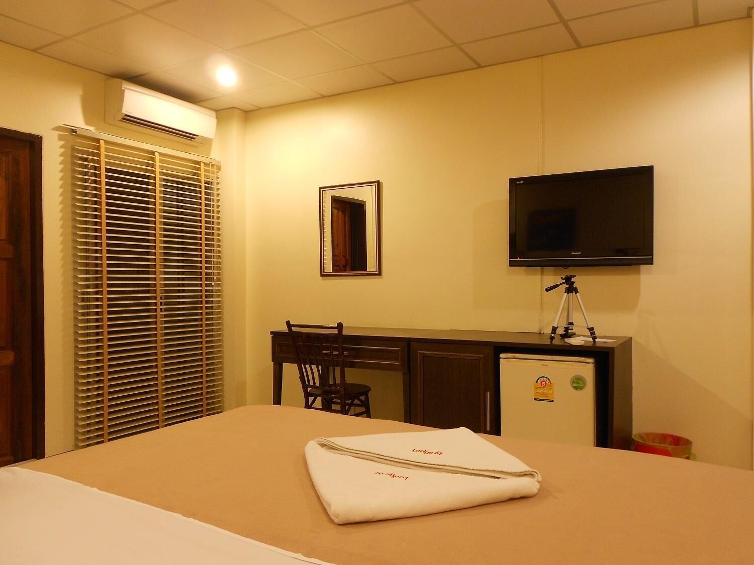 Quarto de hotel com uma cama, escrivaninha, cadeira, televisão e pequeno frigorífico.
