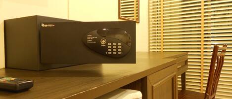 A hotel room with a minibar, a remote control, a wooden chair, and a window with blinds.