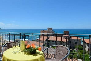 A balcony with a table set for two, overlooking a coastal view.