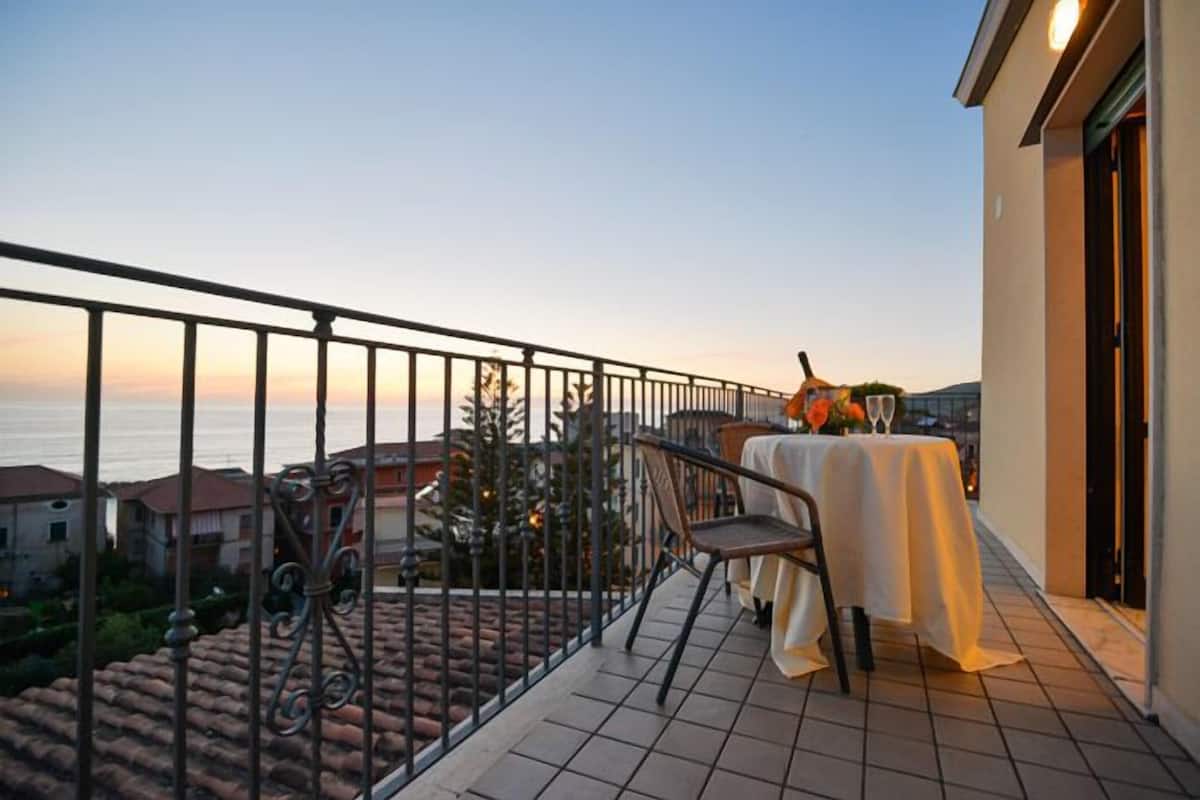 Ein Balkon mit Tisch für zwei Personen, Blick auf einen Wohnort und das Meer.