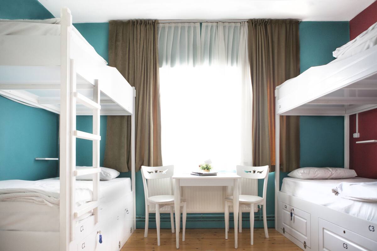 Una habitación con literas, un escritorio, dos sillas y una ventana con cortinas.