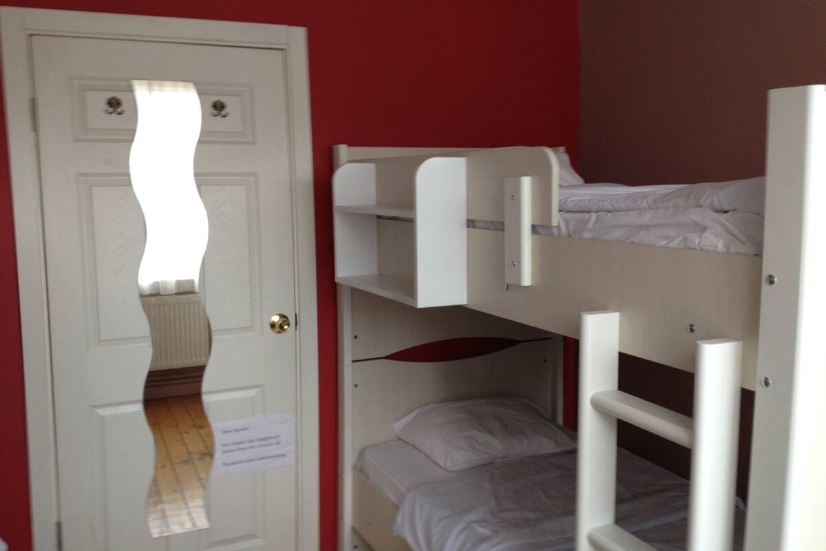Una habitación con literas, una puerta blanca y una pared roja.