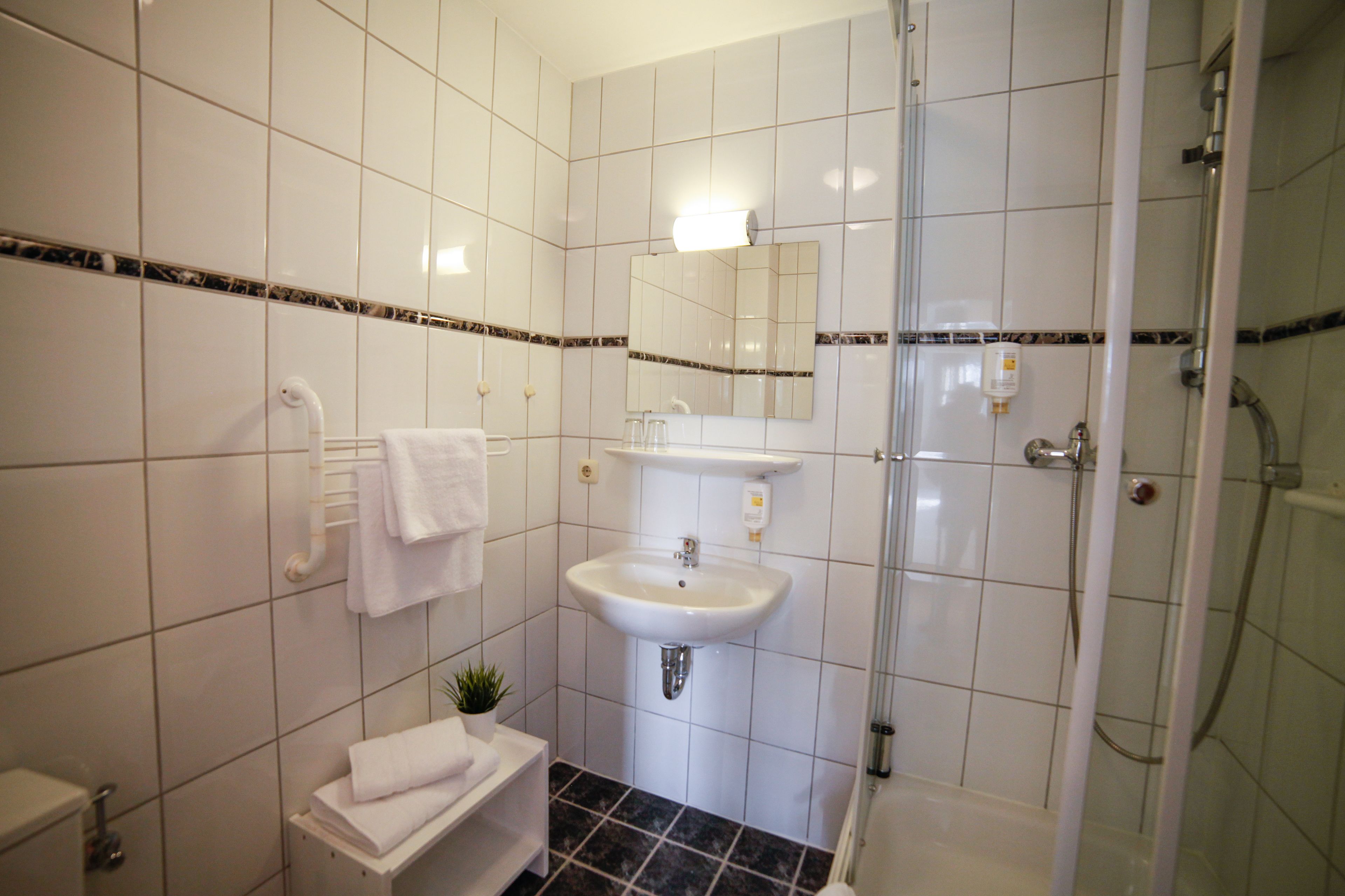 Une salle de bain avec des carreaux blancs, un lavabo, un miroir, un porte-serviettes et une douche.
