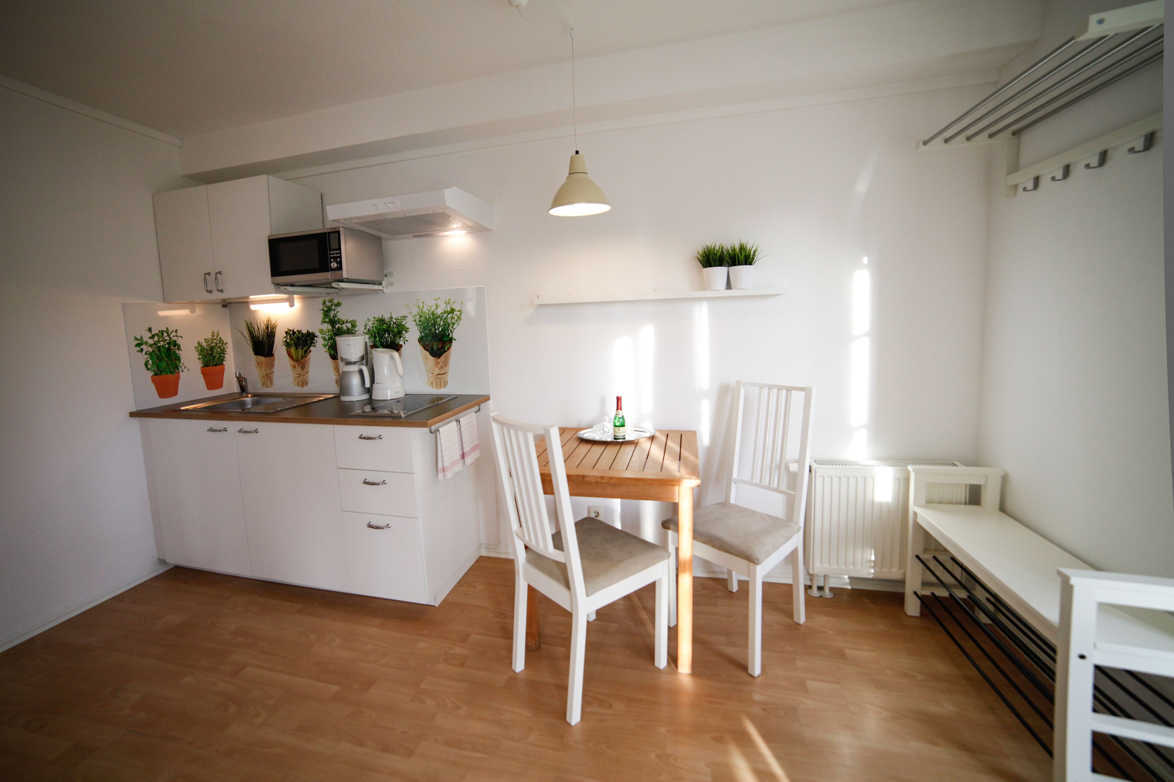 Een moderne keuken met witte kastjes, een houten aanrecht en een eettafel met stoelen. Er staan potplanten op het aanrecht en hangt een lamp boven de tafel.