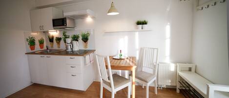 Een moderne keuken met witte kastjes, een houten aanrecht en een eettafel met stoelen. Er staan potplanten op het aanrecht en hangt een lamp boven de tafel.