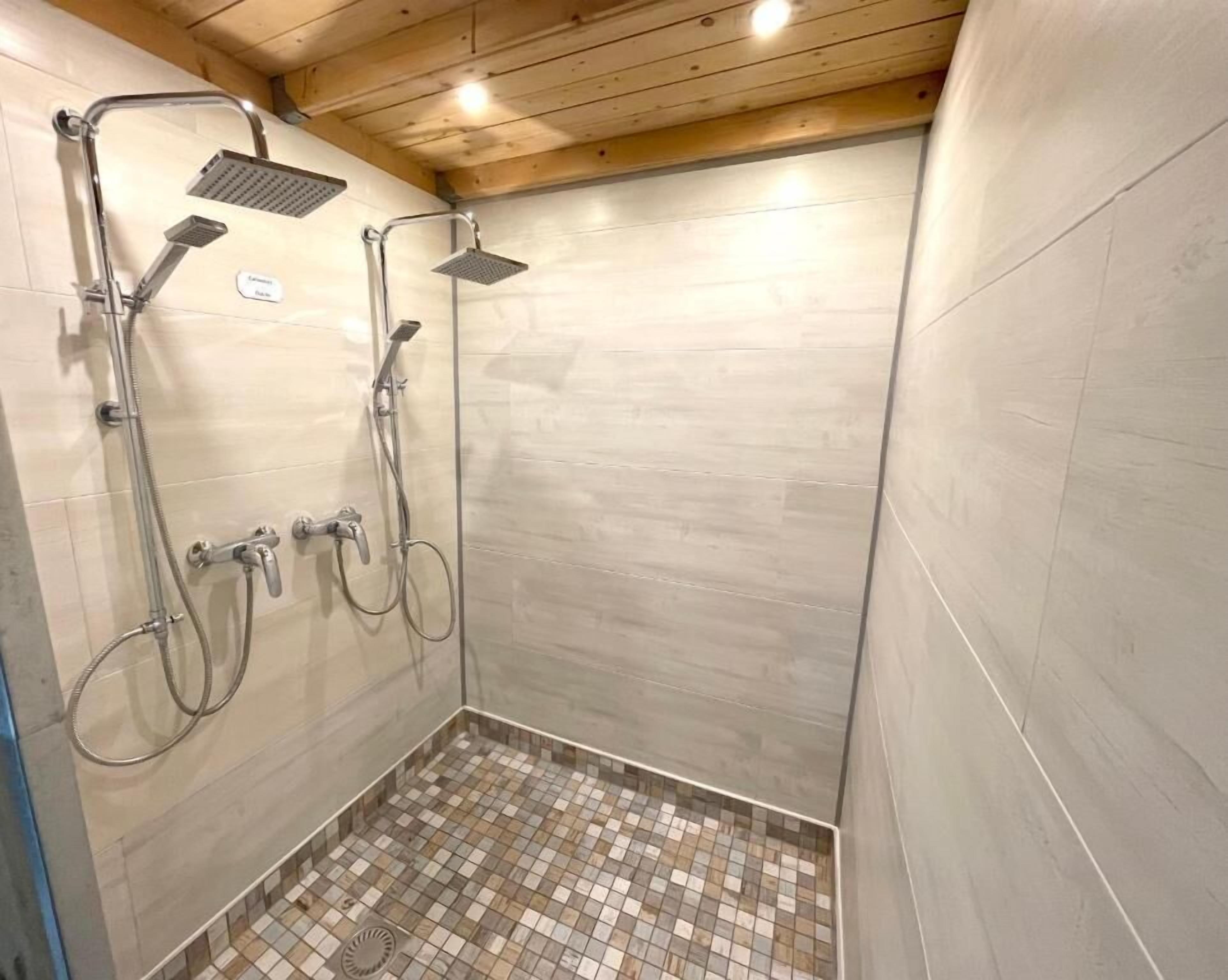 A shower area with a tiled floor, wooden ceiling, and a wall-mounted showerhead.