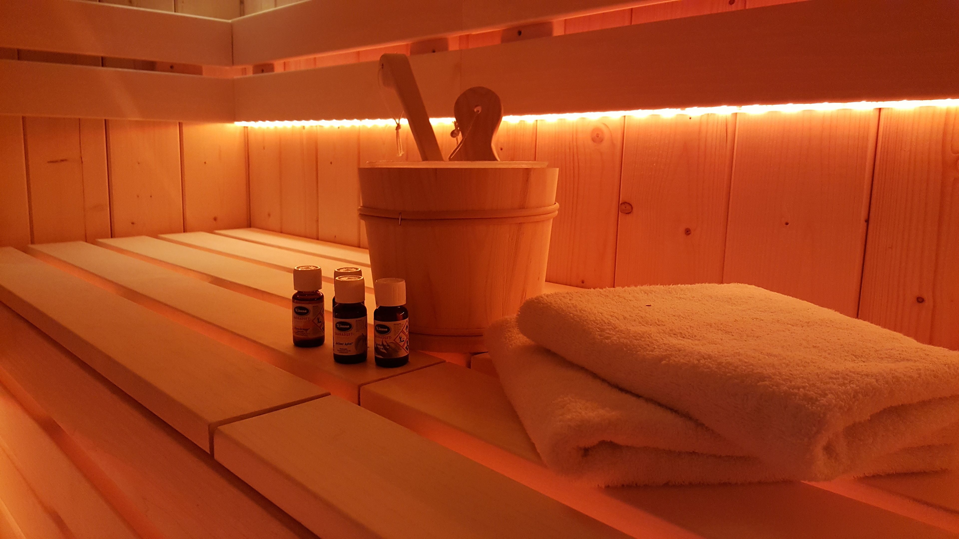 Un sauna en bois avec des bancs, un seau contenant des outils en bois et des bouteilles d’huiles.