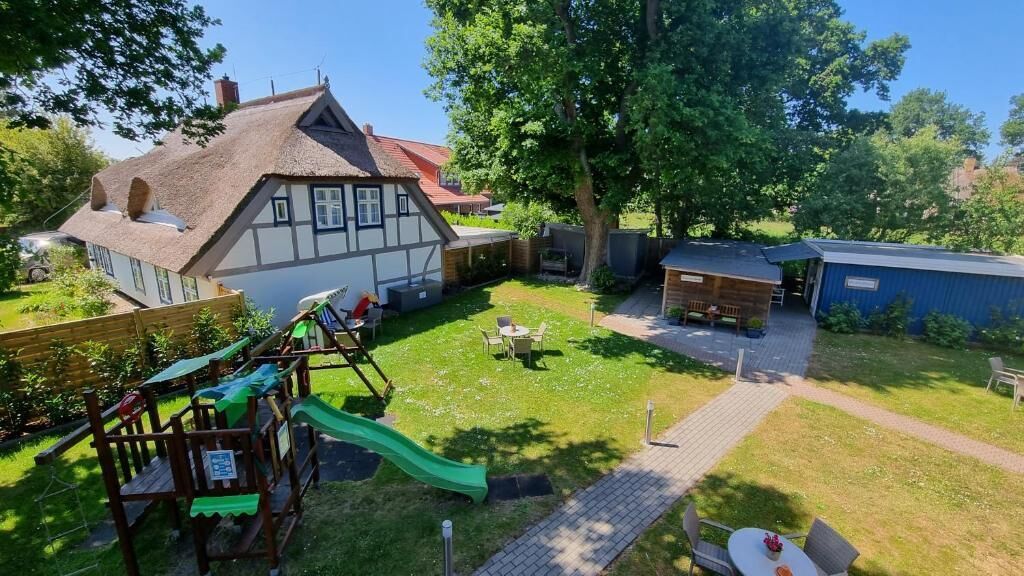 A residential property with a thatched-roof house, a play area with a slide, and a paved patio.