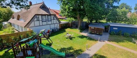 A residential property with a thatched-roof house, a play area with a slide, and a paved patio.