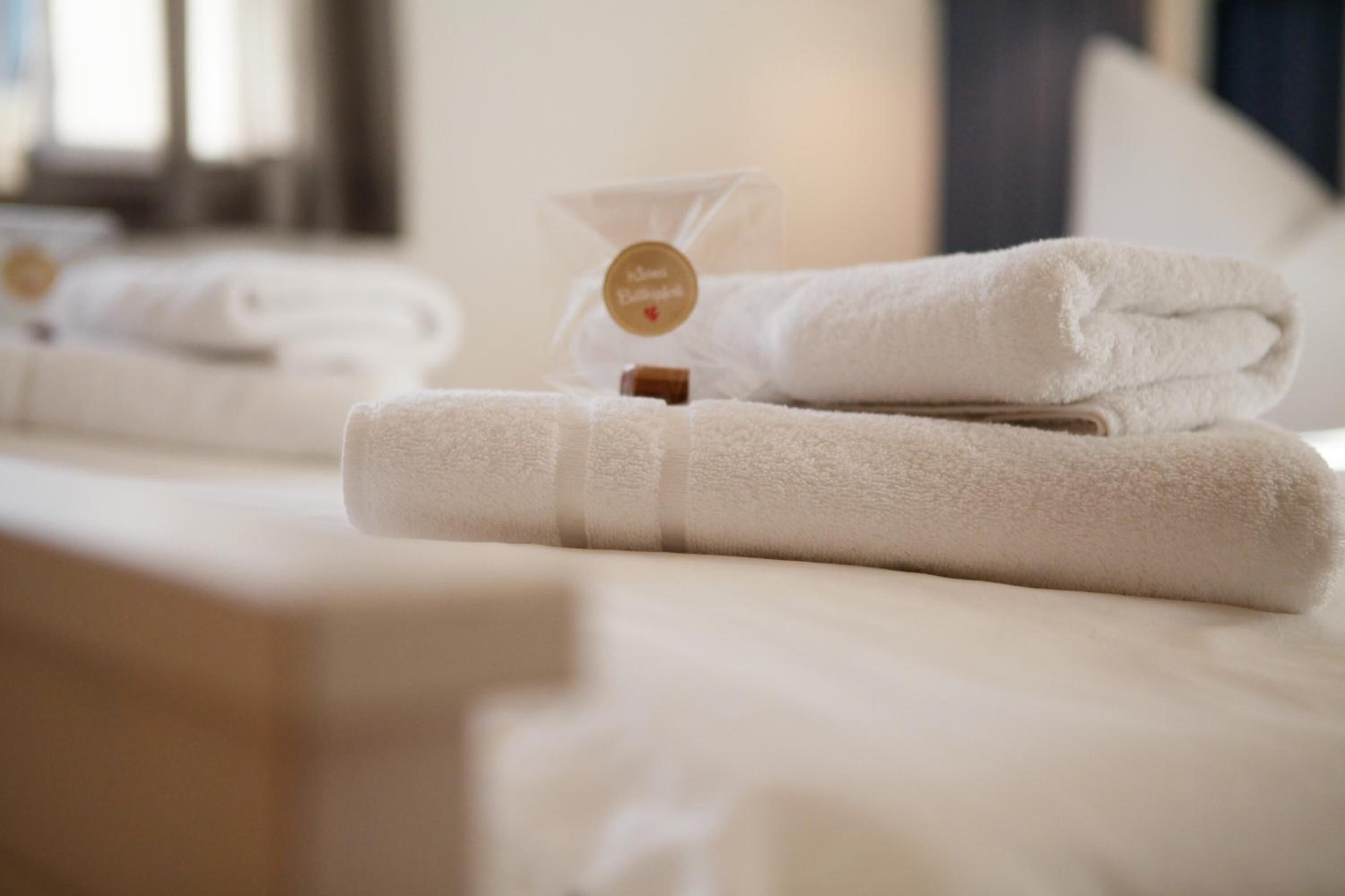 Neatly folded white towels on a bed with a small bottle and a tag.