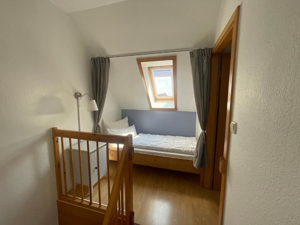 Une chambre avec un lit superposé, une petite fenêtre et une porte donnant sur une autre pièce.