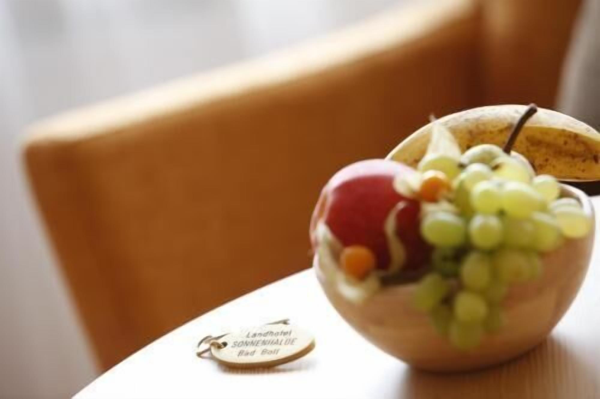 Uma tigela de madeira com uvas, uma maçã vermelha e uma banana sobre uma mesa.