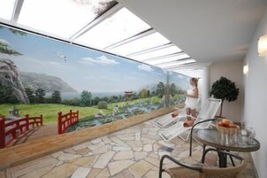 Une pièce avec une grande fresque représentant un paysage, un sol en pierre, une table en verre avec un bol et une chaise.