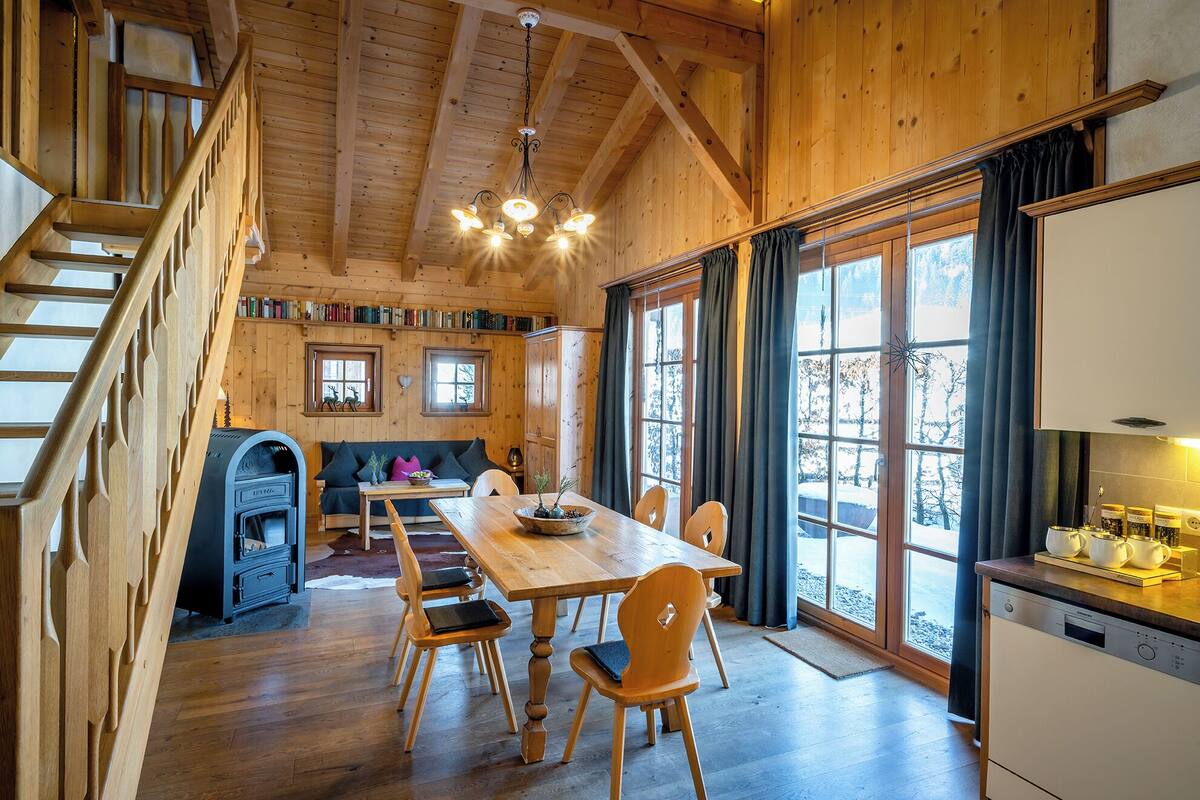 A wooden cabin interior with a dining area, kitchen, and a staircase.