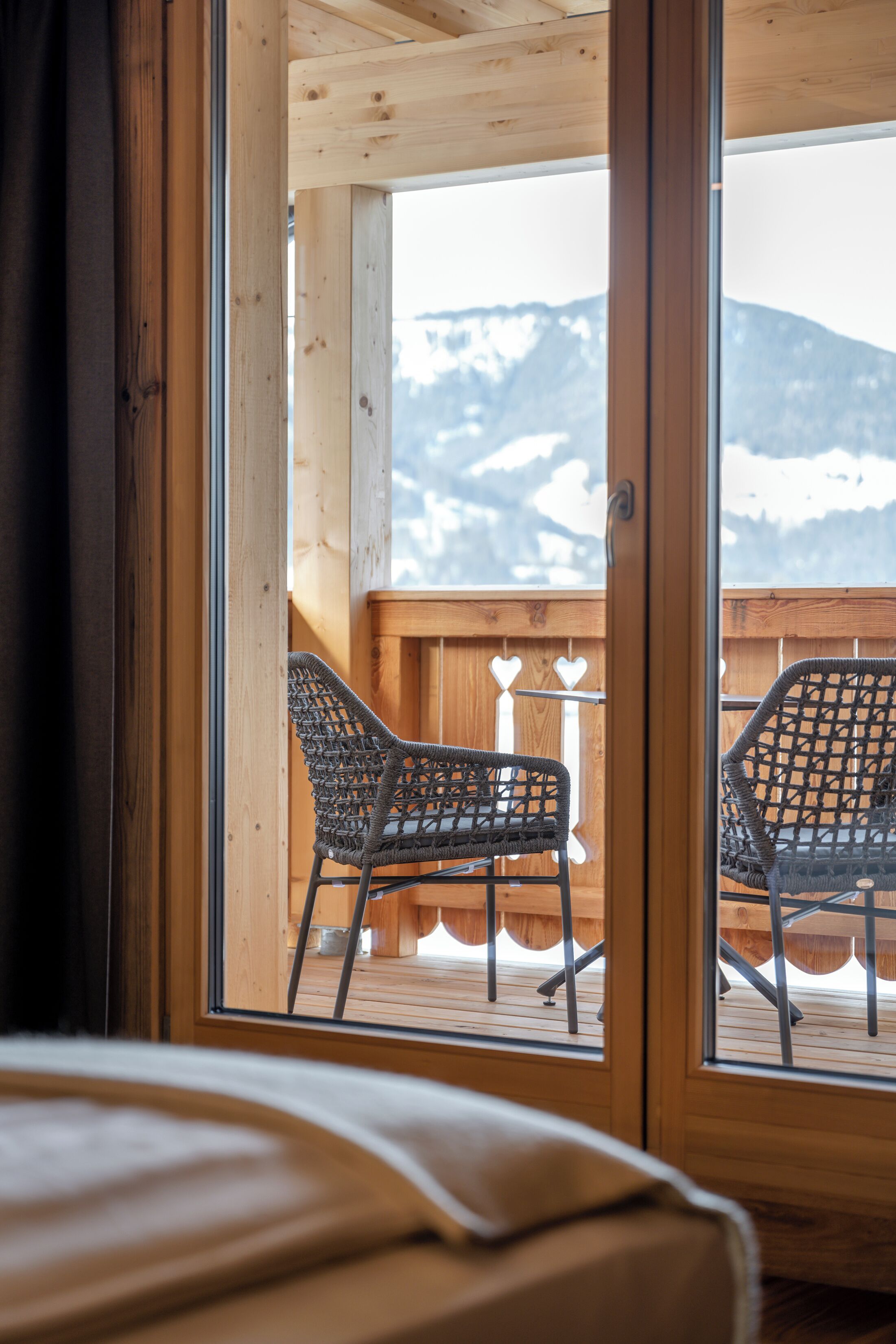 Un balcón de madera con dos sillas de mimbre y una mesa, con vista a una montaña nevada.