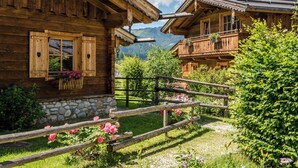 A wooden chalet with a stone foundation, a wooden fence, and a garden with flowers. - Almdorf Almlust (Flachau)