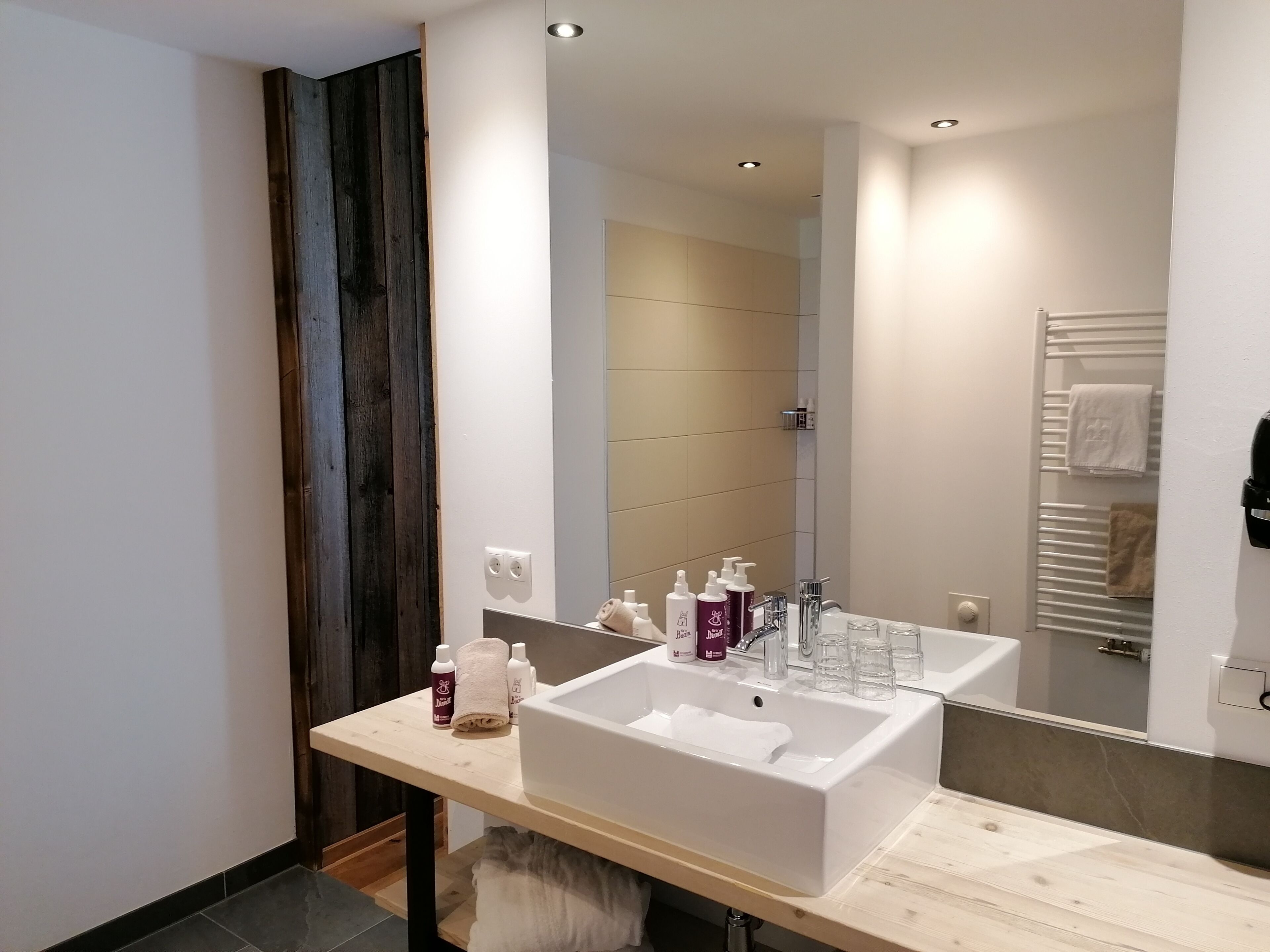 Un baño moderno con un espejo grande, dos lavamanos y un perchero para toallas.