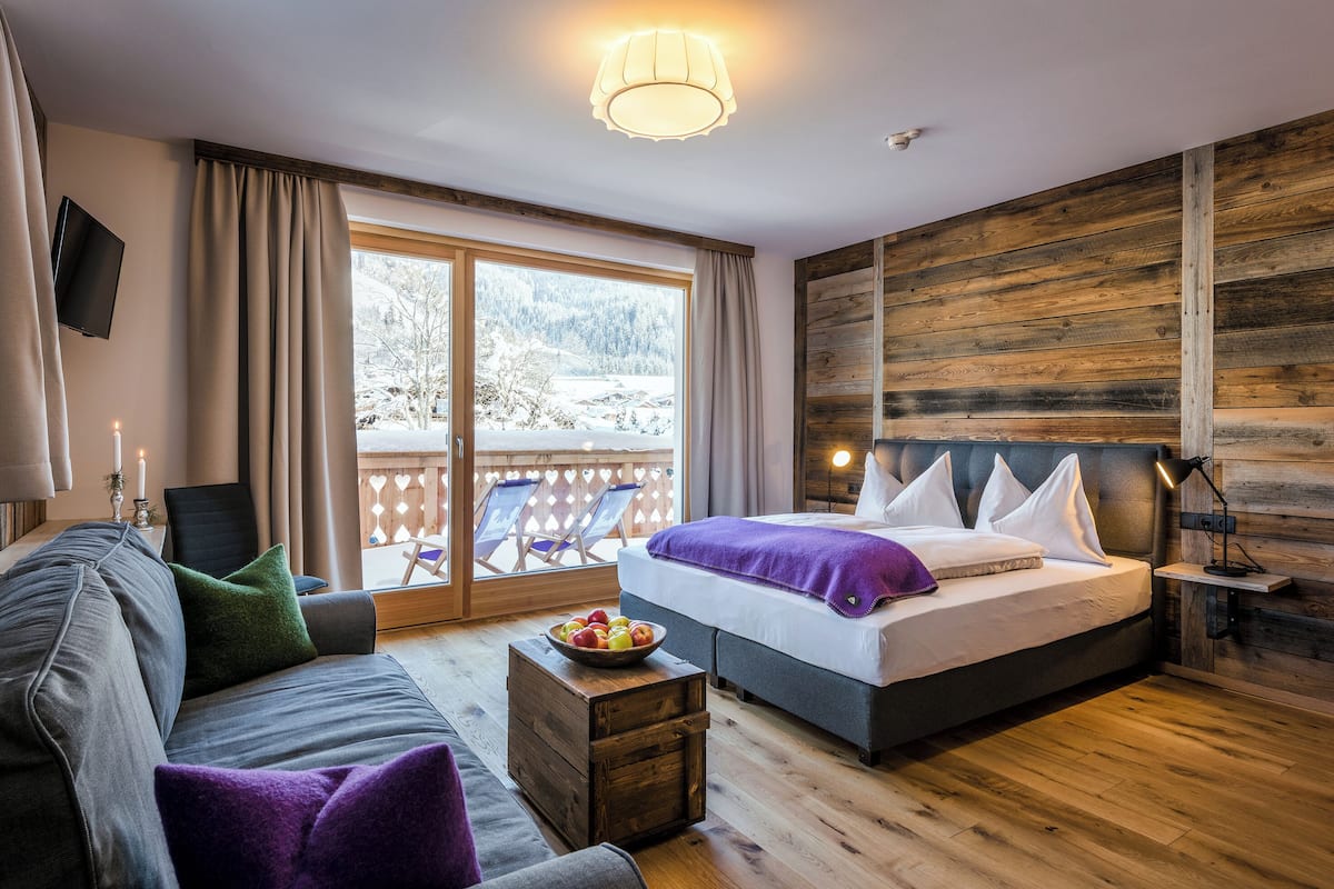 A bedroom with a bed, a sofa, a small table with fruit, a TV, and a view of a snowy landscape.