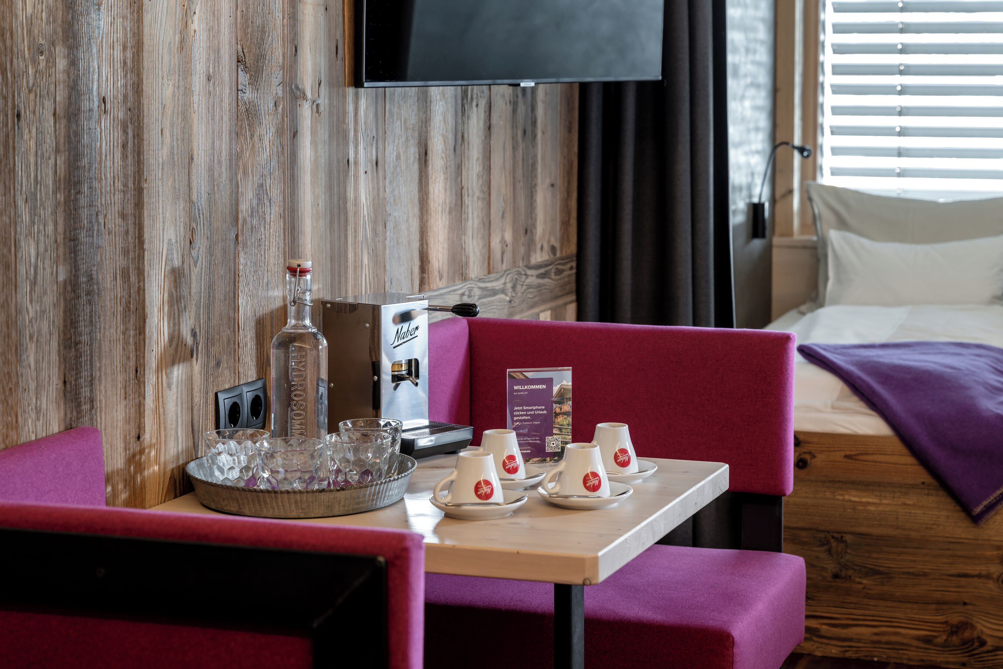 A hotel room with a wooden wall, a TV mounted above a bed, a table with a tray of glasses, and a sign on the wall.