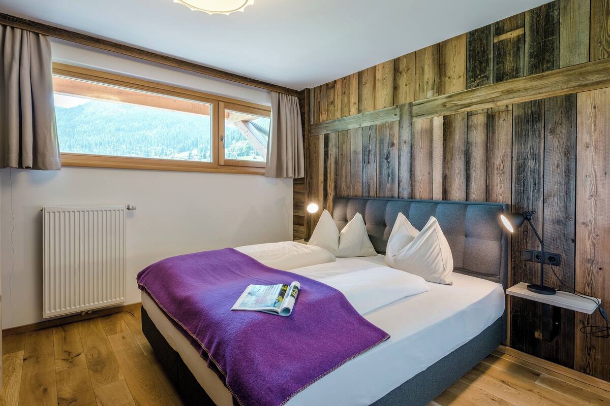 A bedroom with a bed, a window, a radiator, and a wooden wall.