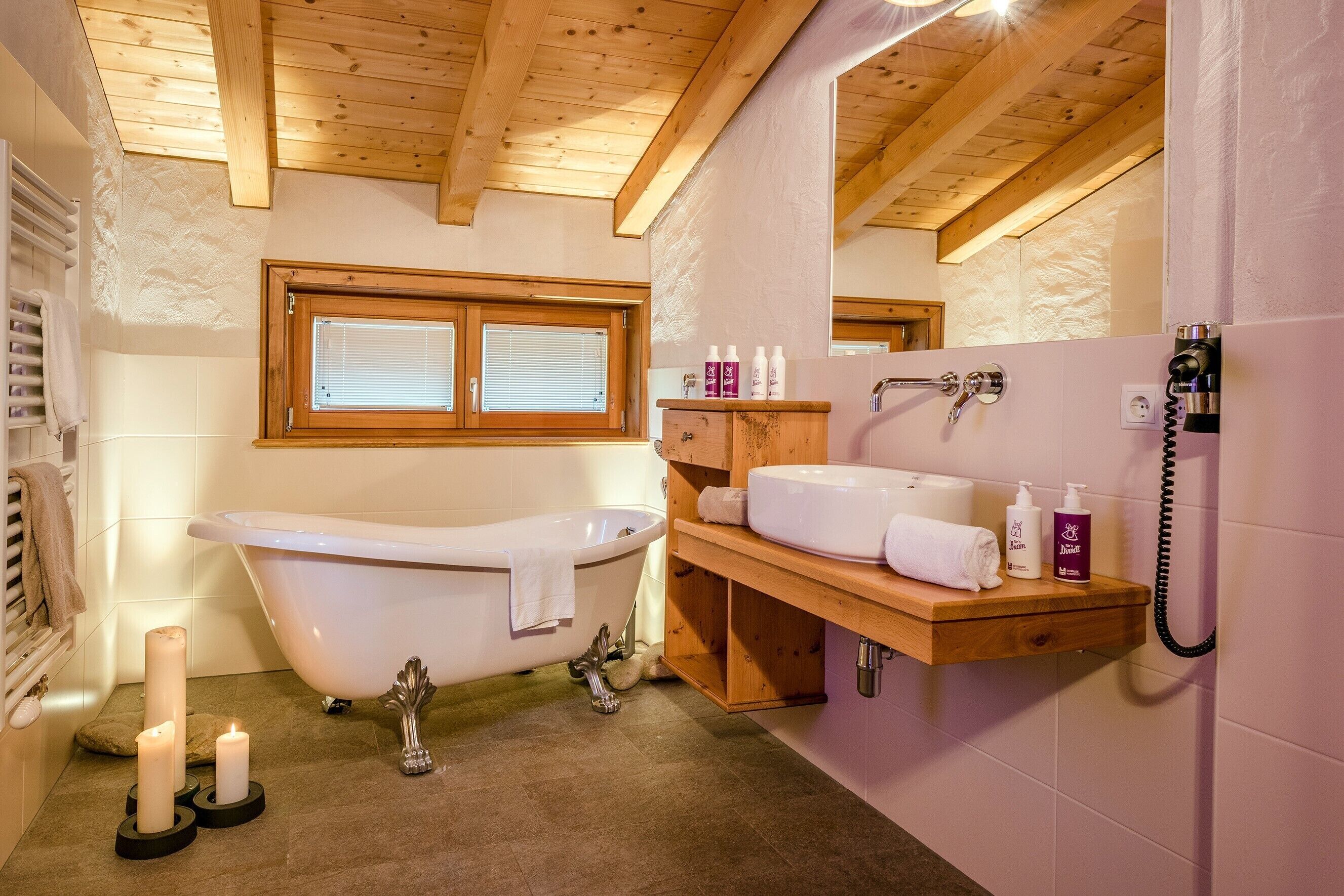 Une salle de bain avec une baignoire, un meuble-lavabo en bois, un miroir et une fenêtre.