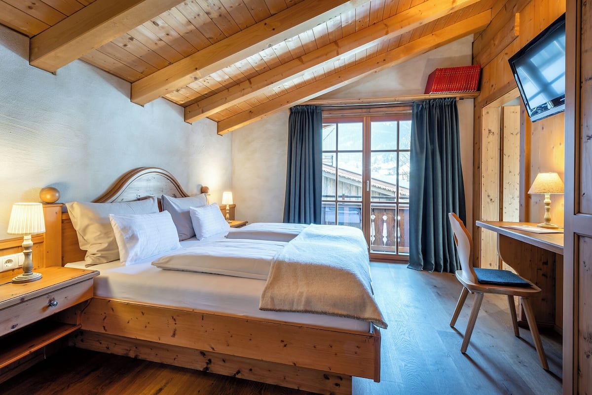 A wooden-framed bedroom with a bed, bedside tables, a desk, and a TV.