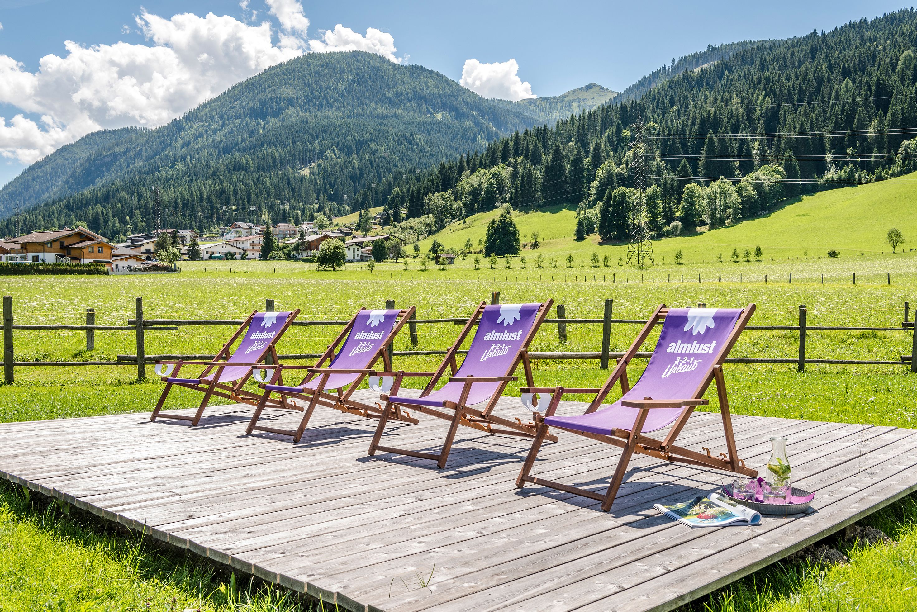 A wooden deck with four purple lounge chairs labeled "almost perfect" and a magazine on the ground.