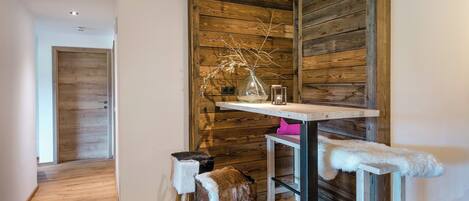 Una habitación con una pared de acento de madera, una pequeña mesa con un florero, y dos taburetes con mantas de piel.