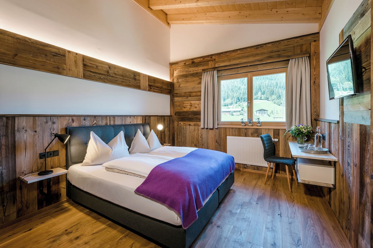 A bedroom with a bed, bedside table, lamp, and a desk with a chair.