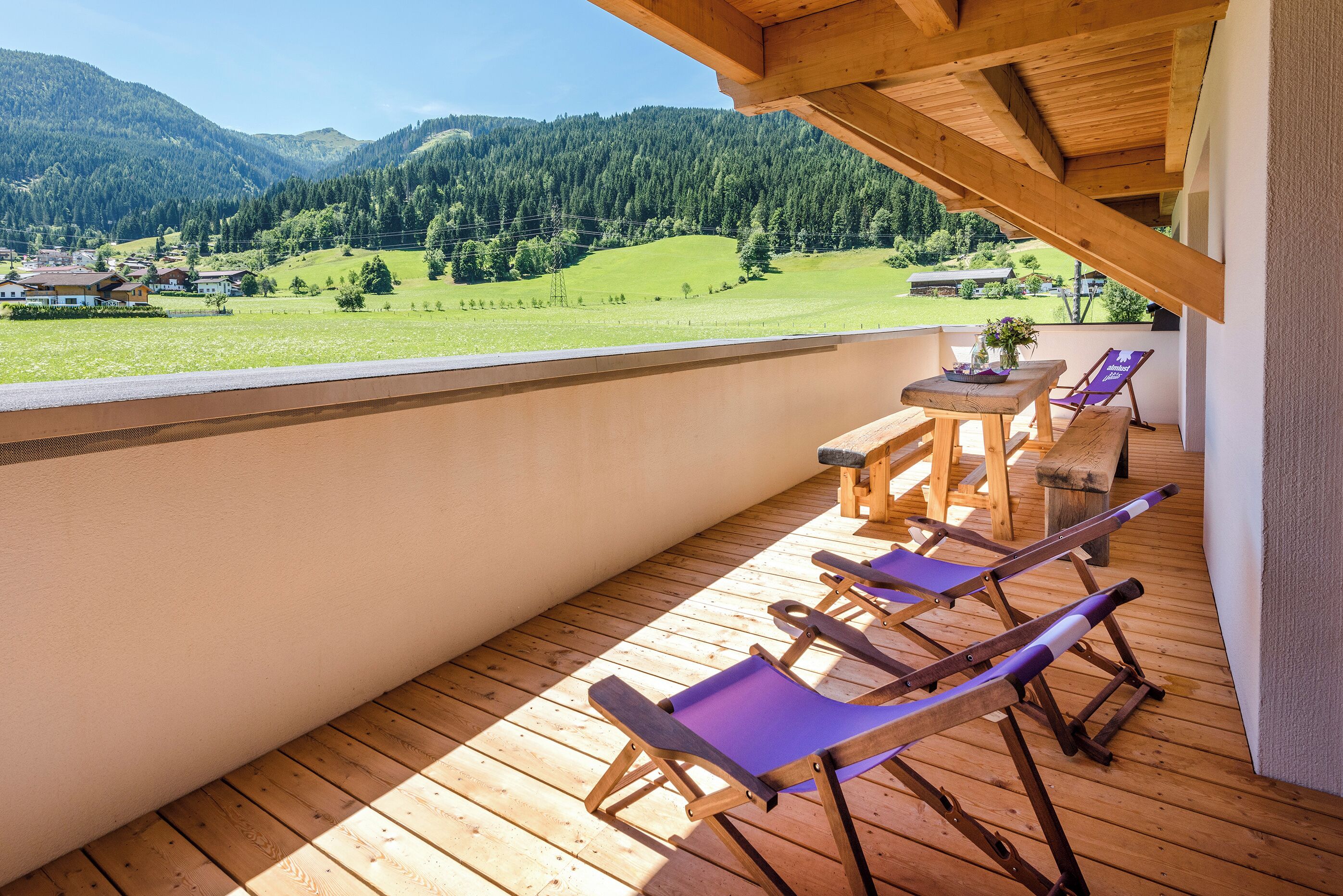 Eine Holzdar Terrasse mit Tisch und Stühlen mit Blick auf ein grünes Tal und Berge.