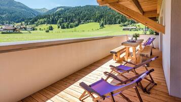Eine Holzdar Terrasse mit Tisch und Stühlen mit Blick auf ein grünes Tal und Berge.