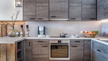 Una cocina moderna con armarios de madera, horno empotrado, cafetera y frutero.