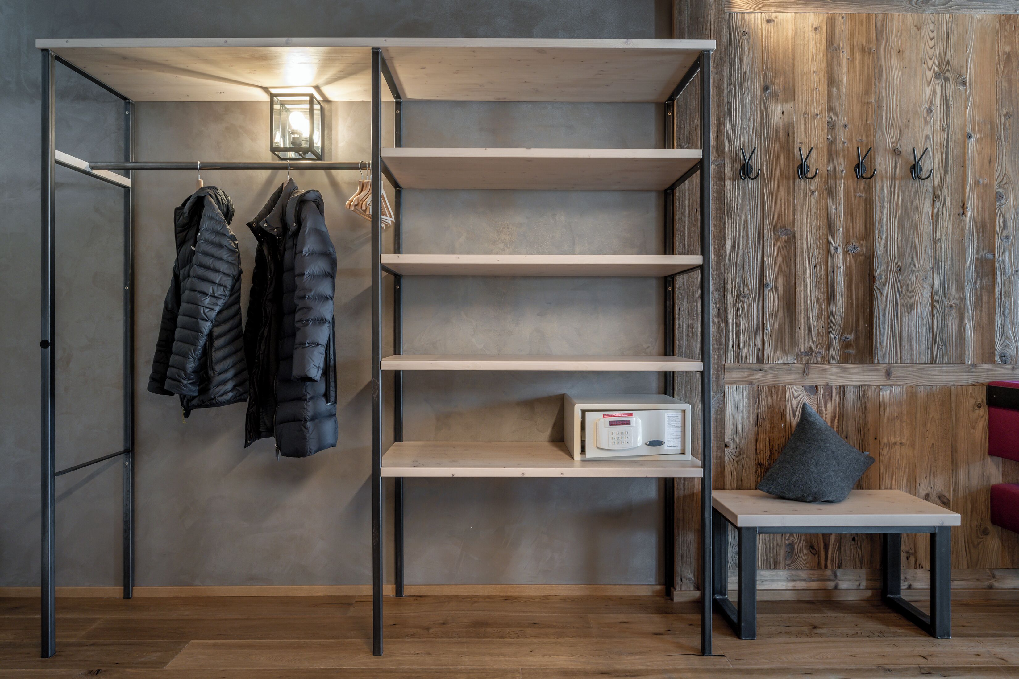 A room with a coat rack, shelves, a table with a pillow, and a wooden wall.