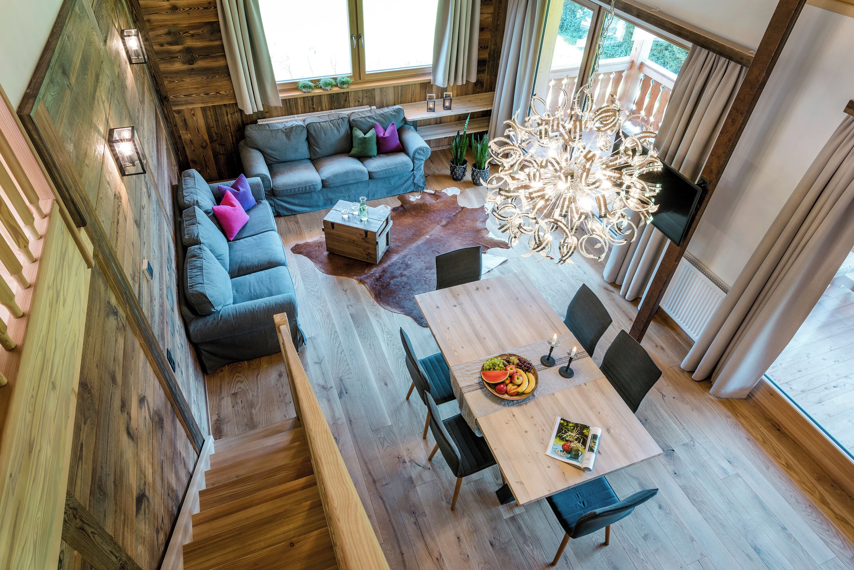A modern interior with a wooden staircase, a sofa set, a dining table with chairs, and a chandelier.