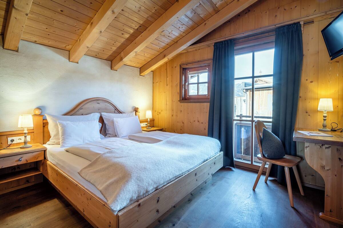 A wooden bedroom with a bed, bedside lamps, a desk, and a chair.