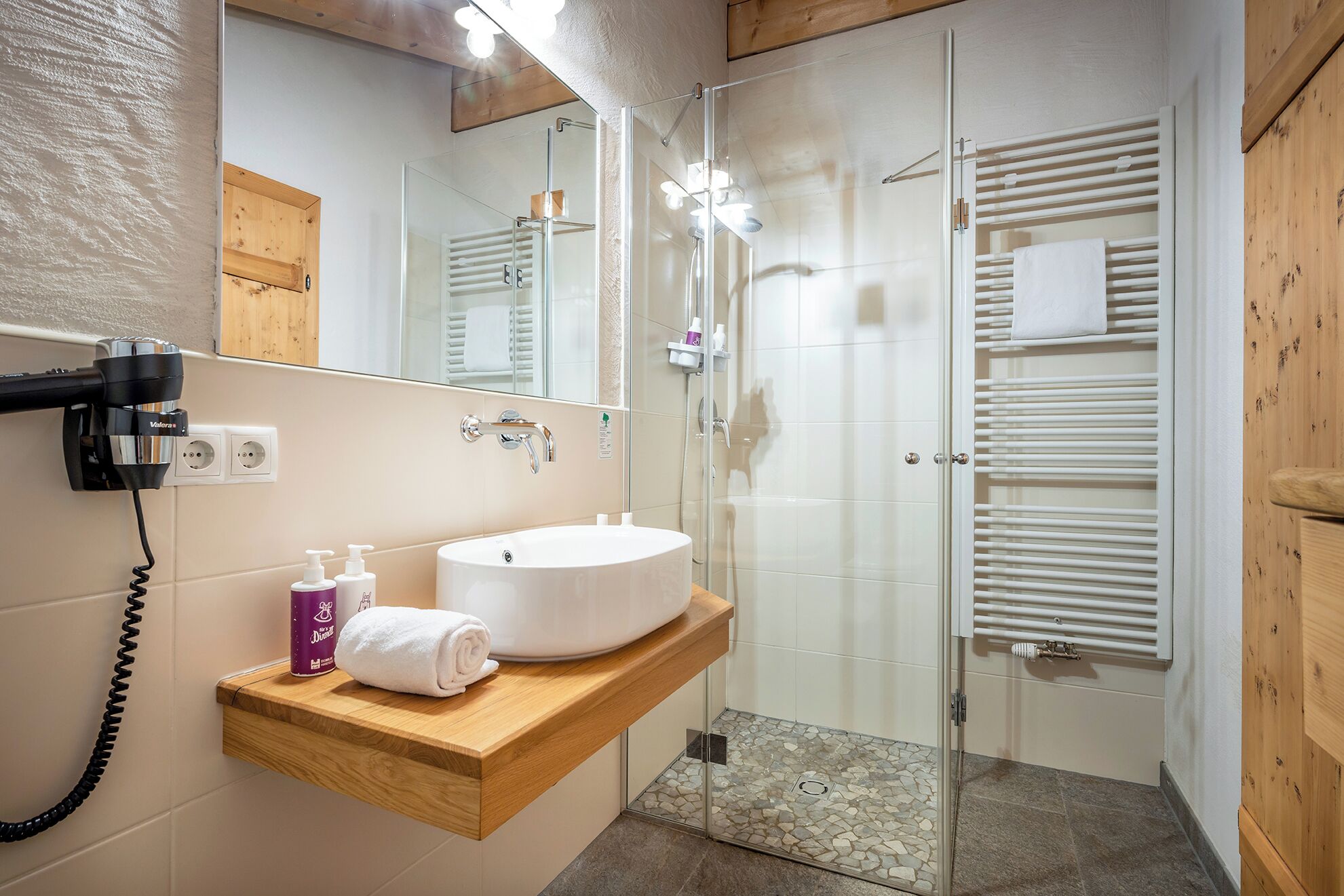 A bathroom with a sink, mirror, towel rack, and shower.