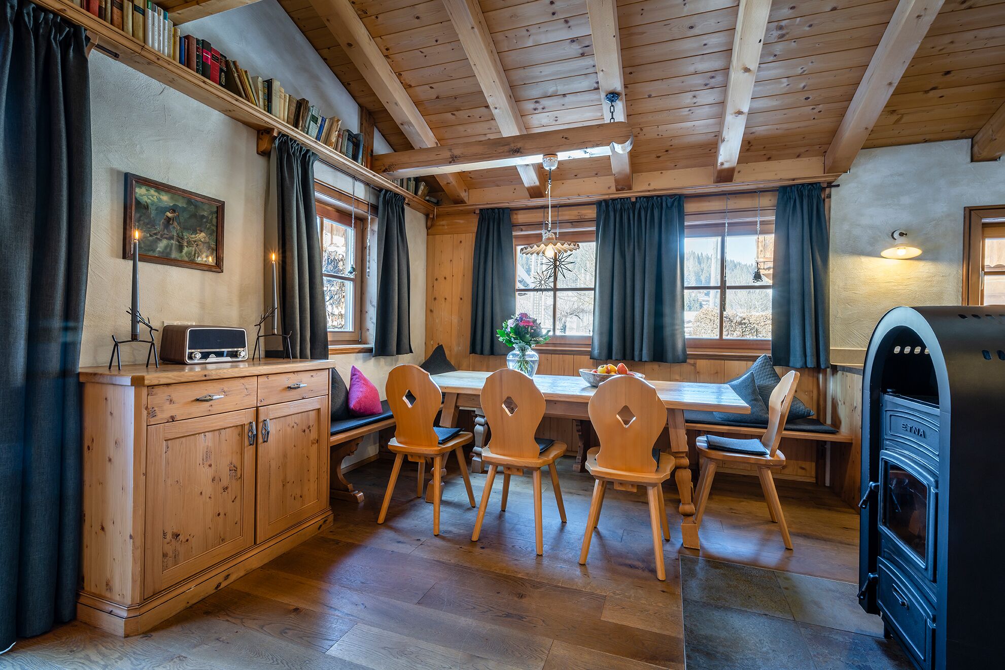 L’intérieur chaleureux d’un chalet avec une table à manger en bois, des chaises, un buffet, une radio et un poêle à bois.
