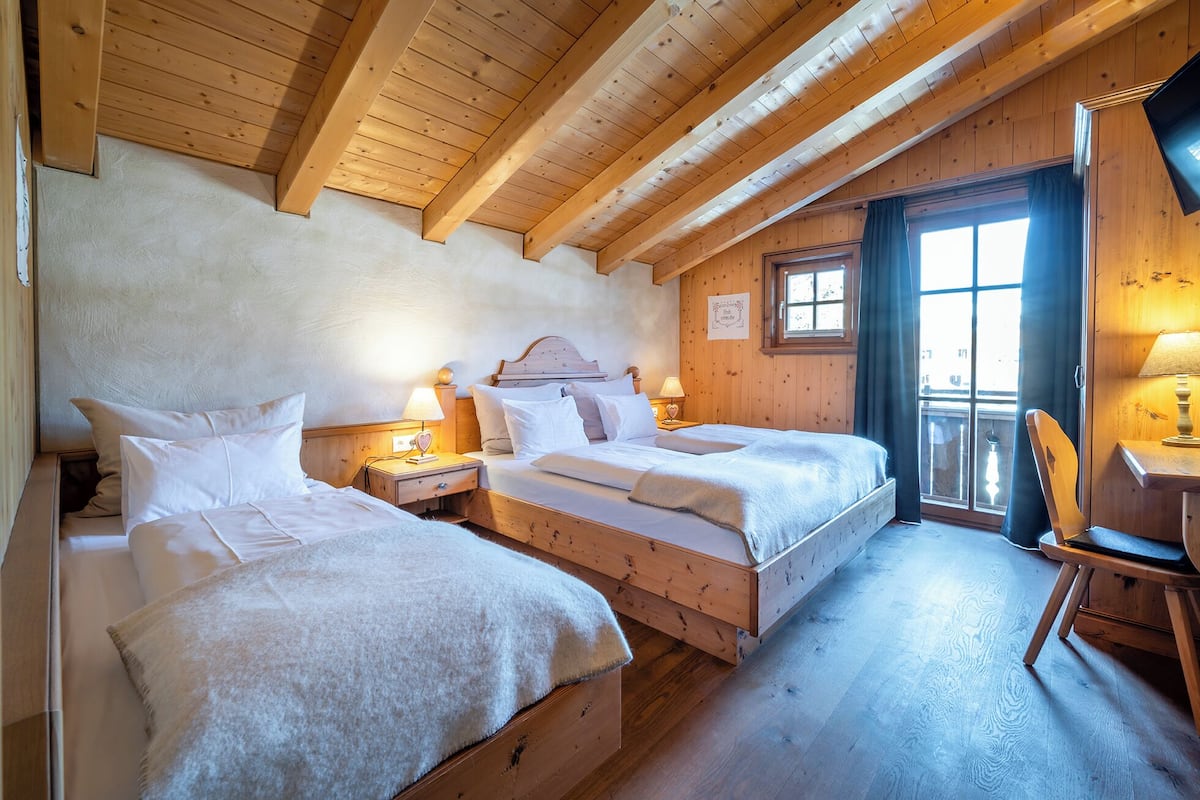 A wooden cabin bedroom with two beds, a desk, and a window.
