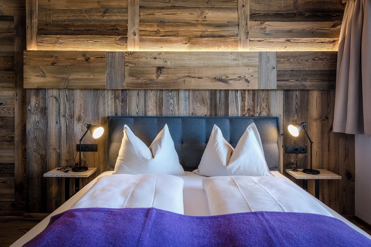 A bed with white linens and a purple blanket, two bedside lamps, and a wooden headboard.