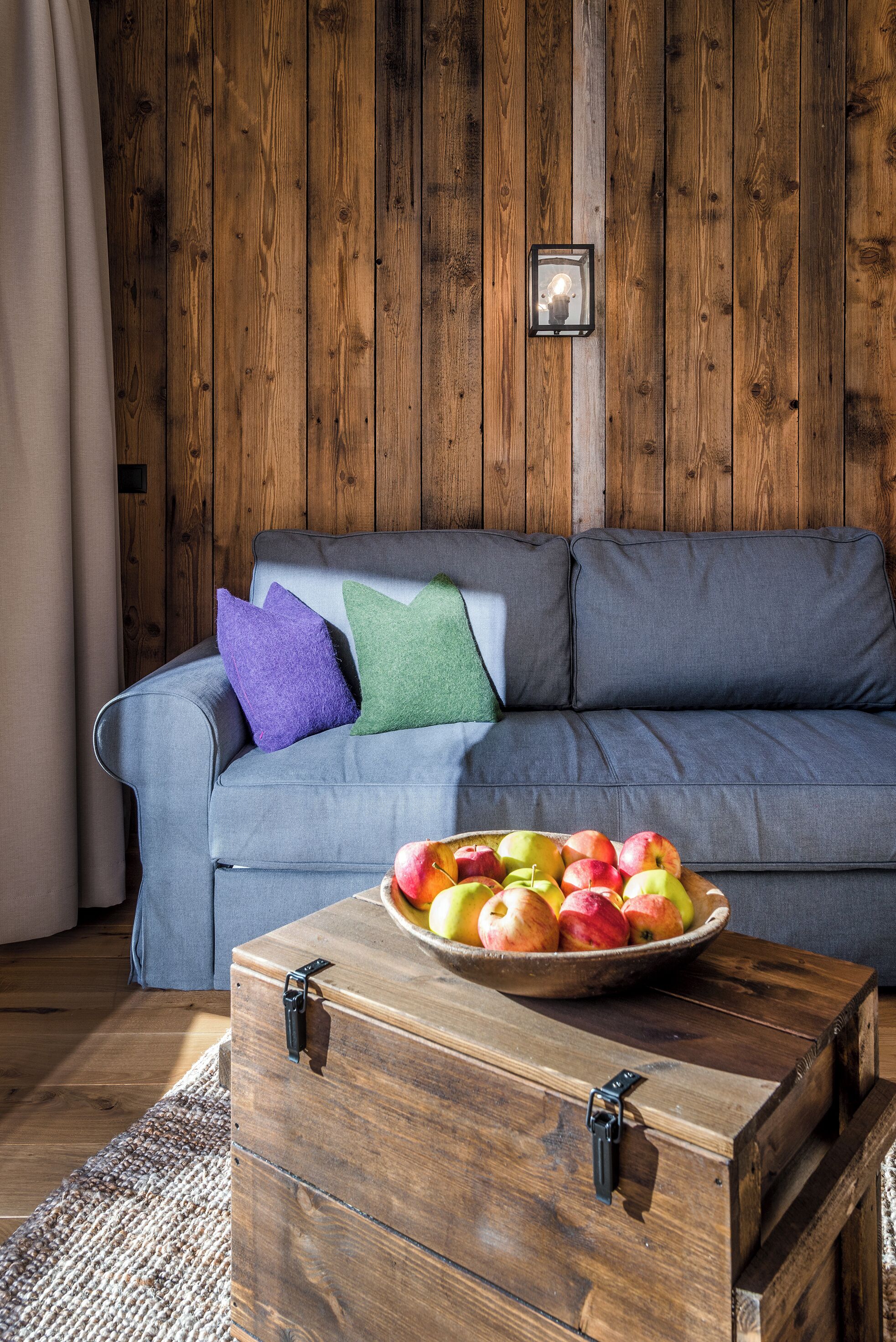 En trævæg, en grå sofa med puder og en træskænk med en skål med frugt.