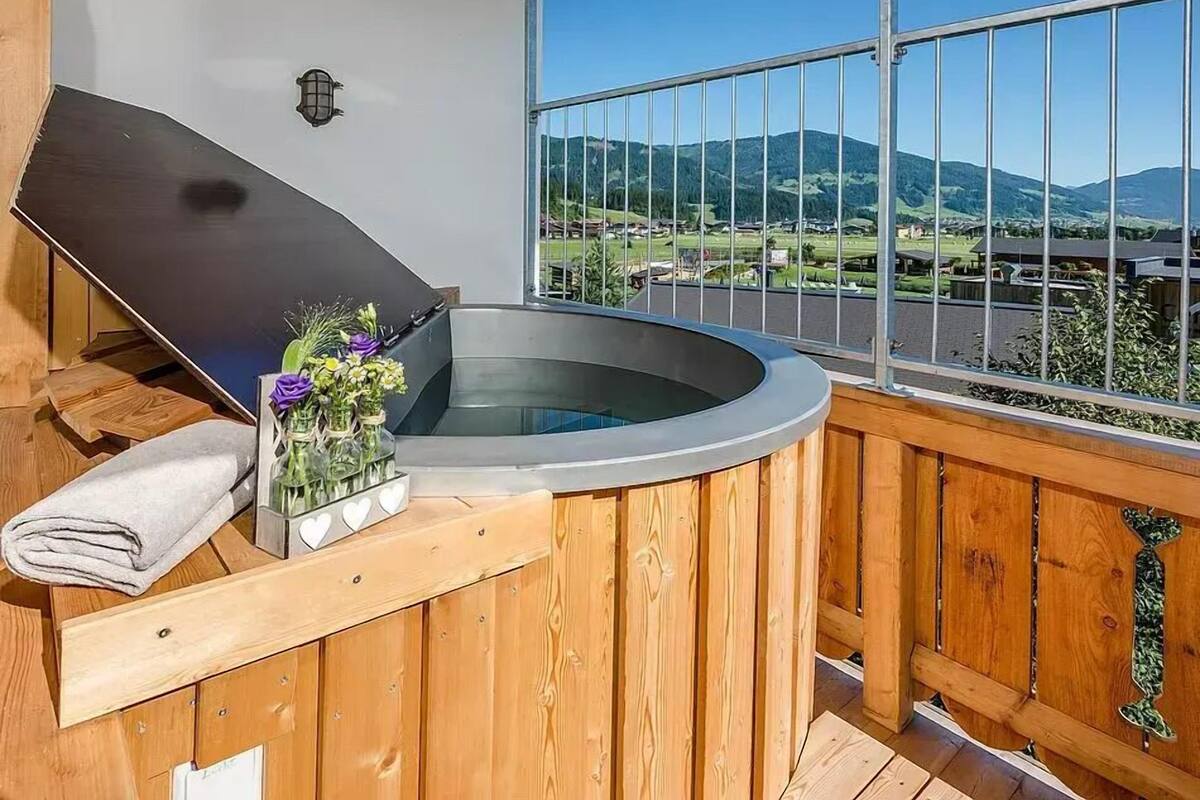 A hot tub on a wooden deck with a view of a valley and mountains.