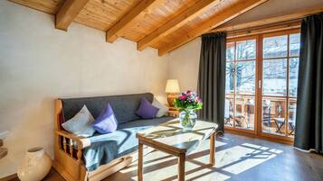 Una habitación acogedora con techo de madera, un sofá con cojines, una mesita con un florero y un ventanal con cortinas.
