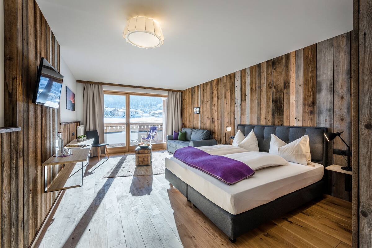 A modern bedroom with a large bed, a desk, a TV, and a view of the outdoors.
