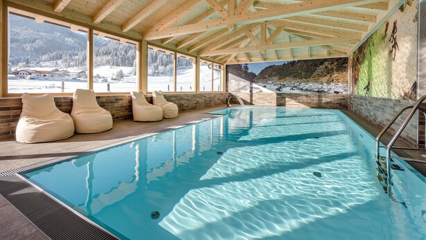 A swimming pool with wooden beams, large windows, and a view of a snowy landscape. - Almdorf Almlust (Flachau)