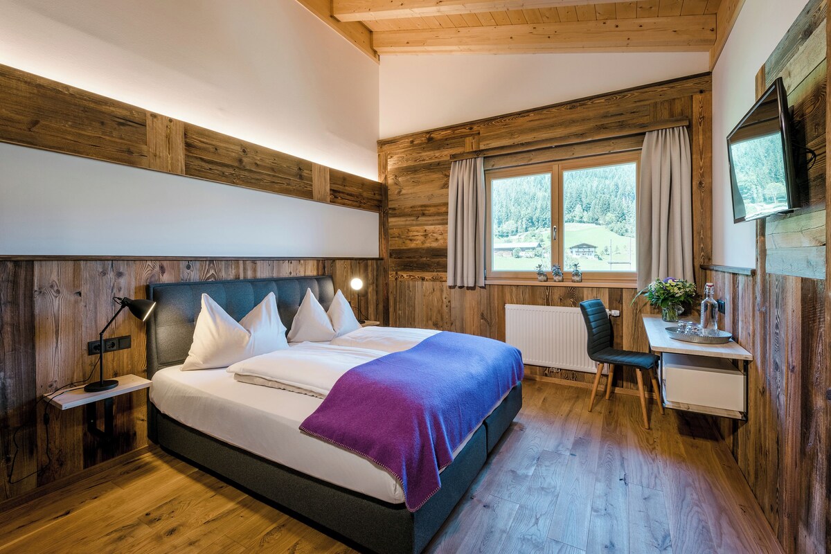 Quarto com cama, mesa de cabeceira, abajur e escrivaninha com cadeira.