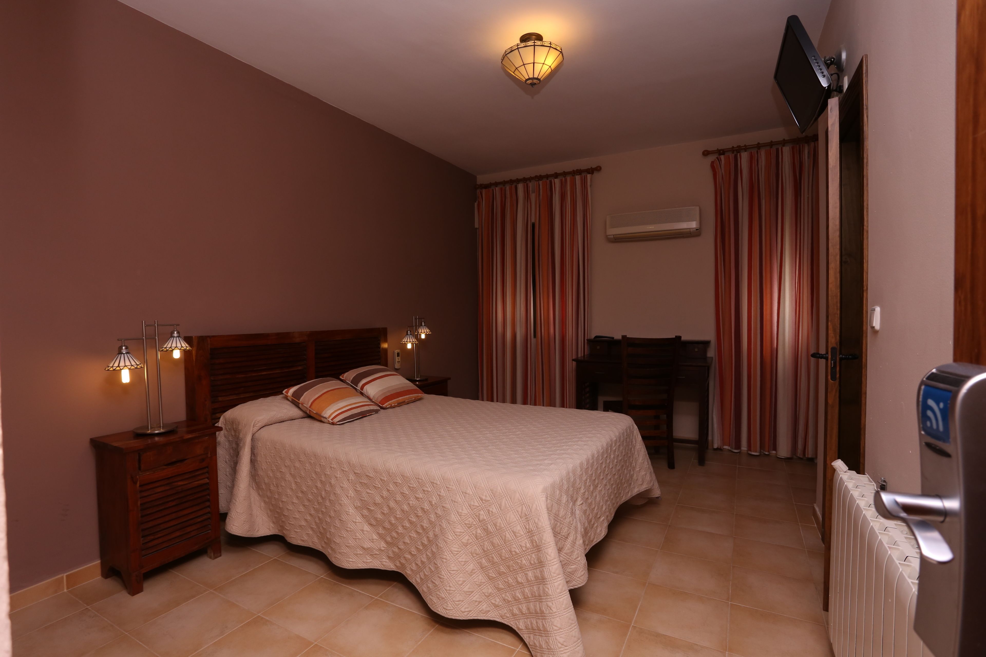 A bedroom with a bed, bedside tables, a desk, and a television.
